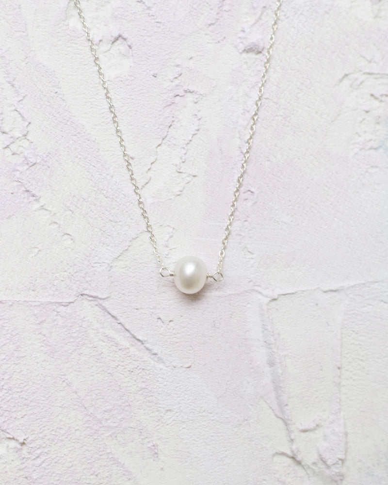 Close flatlay of the pearl drop necklace in silver.