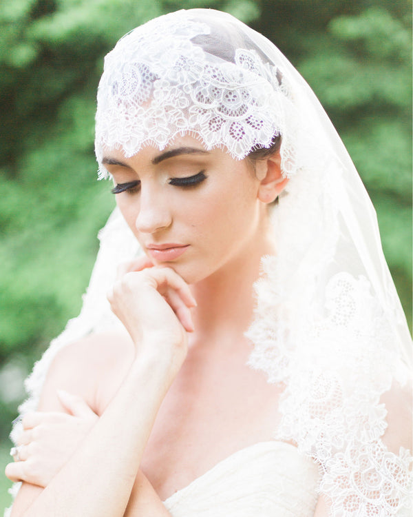 A close view of a model wearing the Analina Mantilla Fingertip Veil, which has a wide Chantilly lace detail all around.