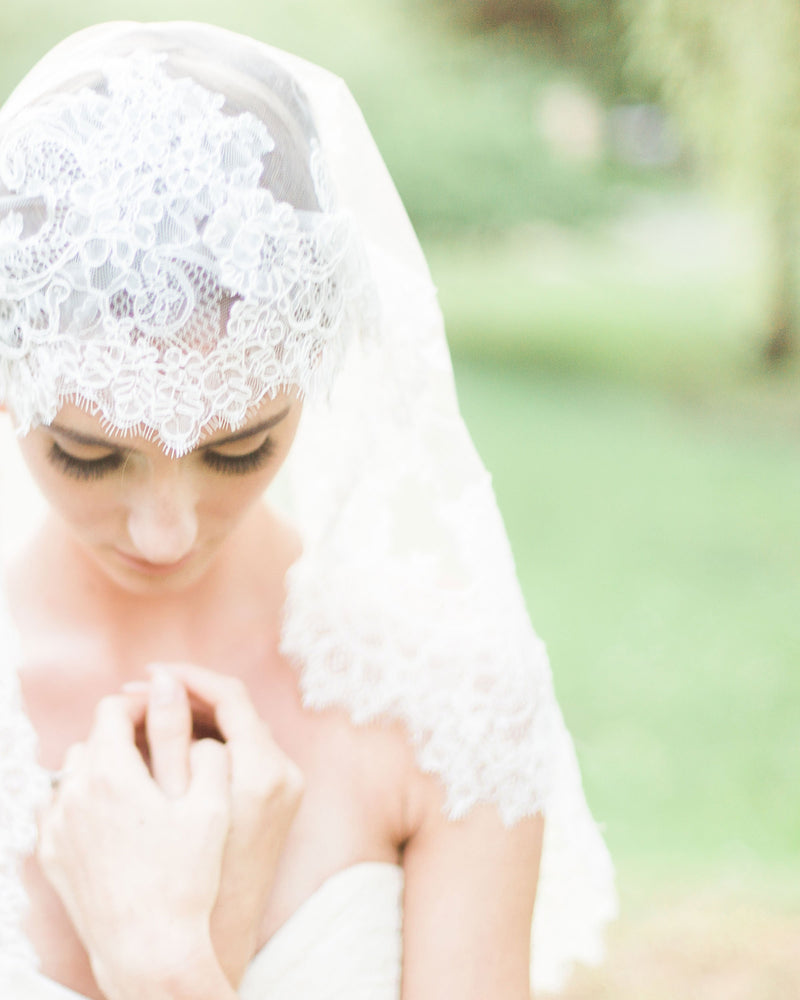 A close view of a bride wearing the Analina Mantilla Fingertip Veil.
