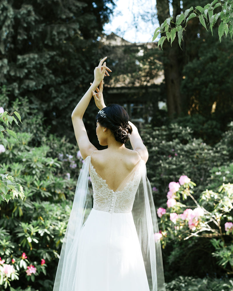 A close back view of a bride wearing the Aster Cape Veil, which attaches to the spaghetti straps of her lace bodice.