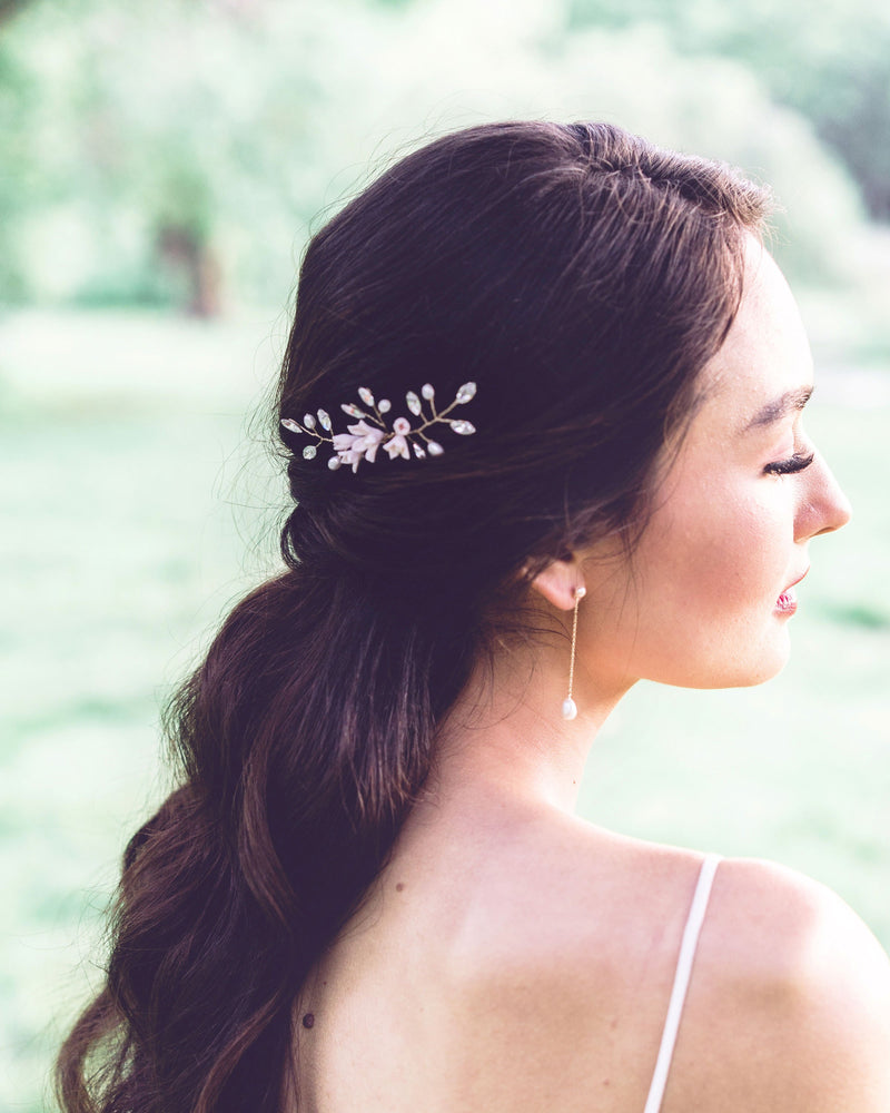 Back view of a dark-haired bride with a half-up hairstyle. She is wearing a hair pin in the side that is gold with blush flowers, pearls, and crystals.