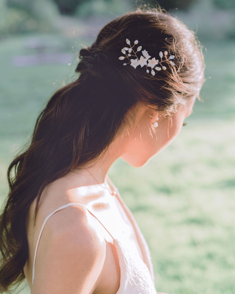 A bride with long dark hair styled into a half updo is wearing a trio of hair pins and pearl drop bridal earrings.