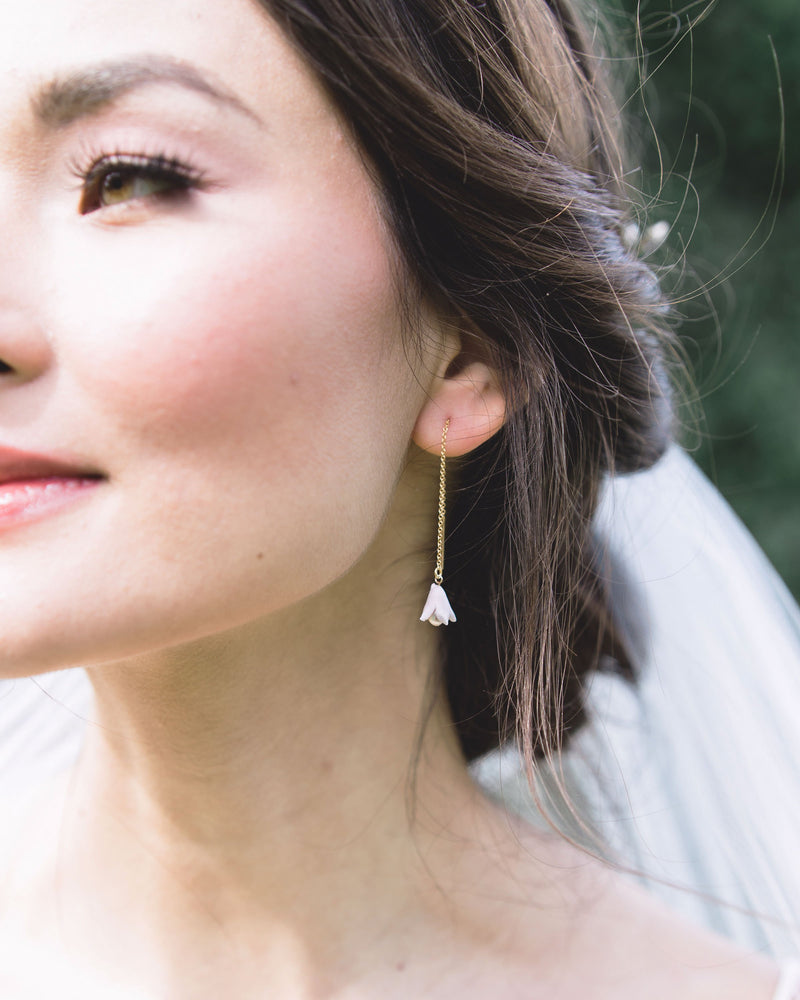 Close-up of a bride wearing a delicate ear threader with a blush flower and pearl at the bottom.