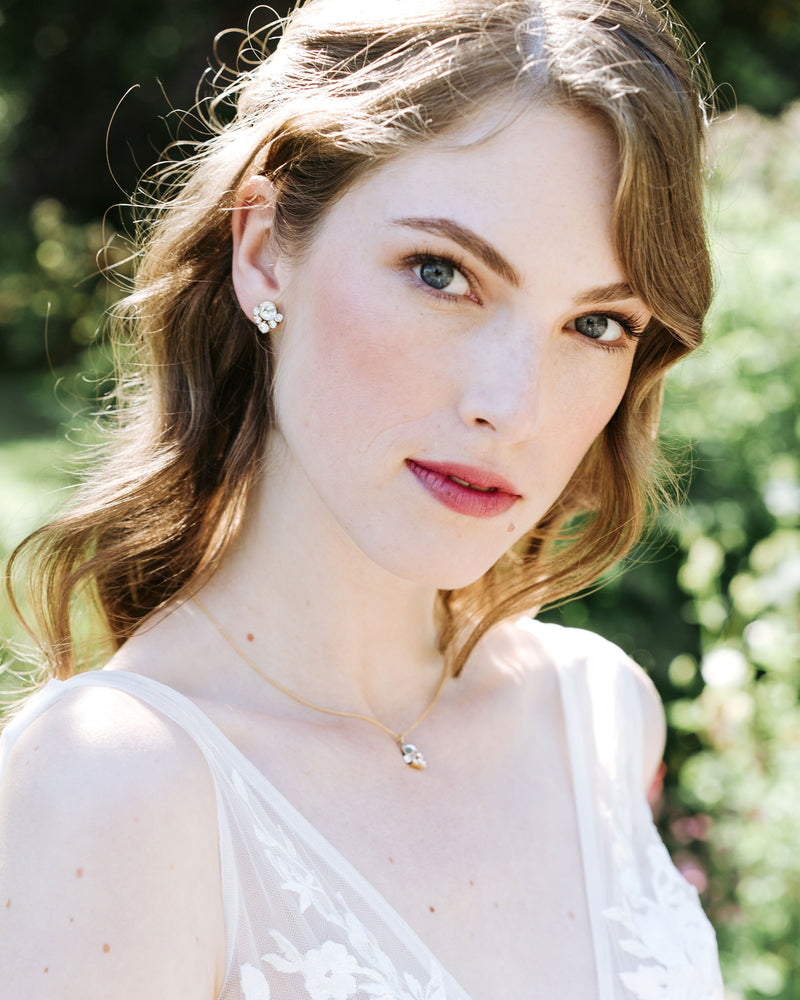 A model gazes into the camera. She is wearing a jewellery set with crystal stud earrings and a delicate gold necklace with a crystal drop.