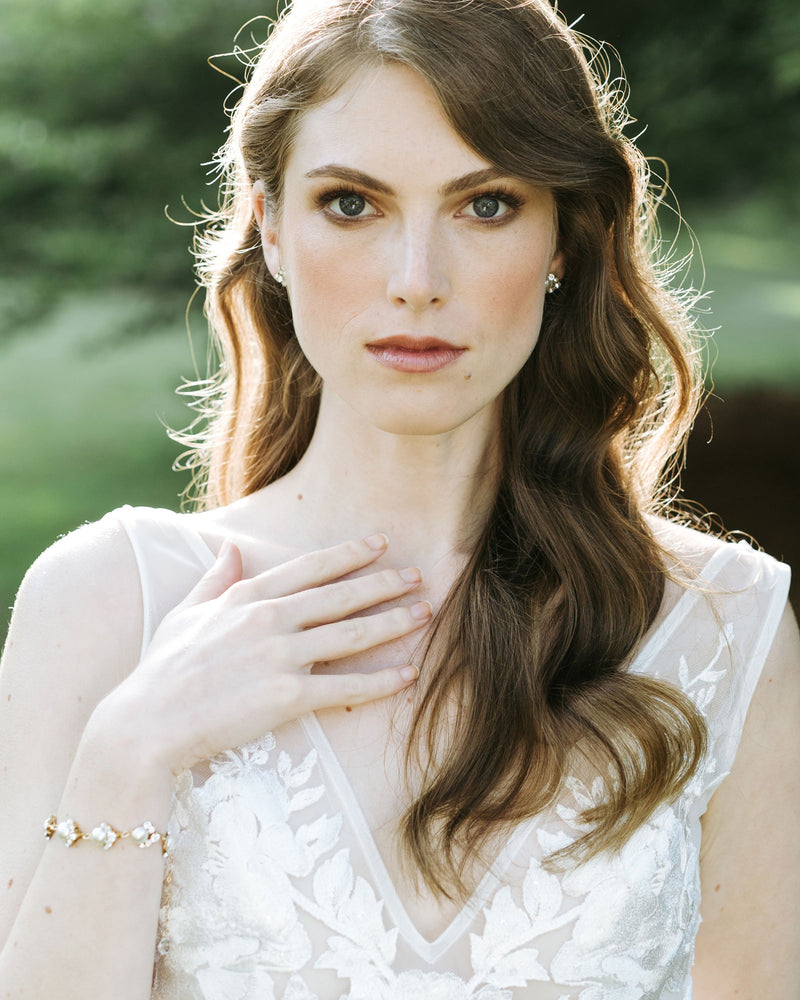 A bride wears the Celestial Pearl Cluster Bracelet in gold and matching pearl stud earrings.
