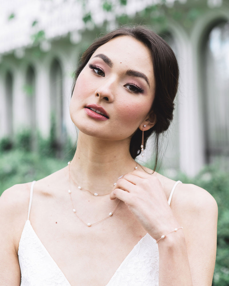 Model with a low bridal updo, wearing the dainty pearl layered necklace in rose gold, paired with the matching dainty pearl bracelet and dainty pearl trio earrings.