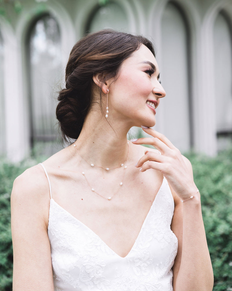 A bride with a low bridal updo wears the Dainty Pearl Trio Earrings, paired with the Dainty Pearl Layered Necklace and Dainty Pearl Bracelet.