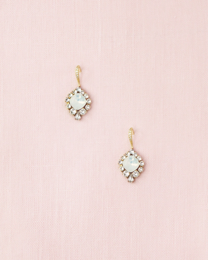 Flatlay of the Enchanted Crystal Drop Earrings in gold with white opal crystal centres. The pave crystal hook version is shown.