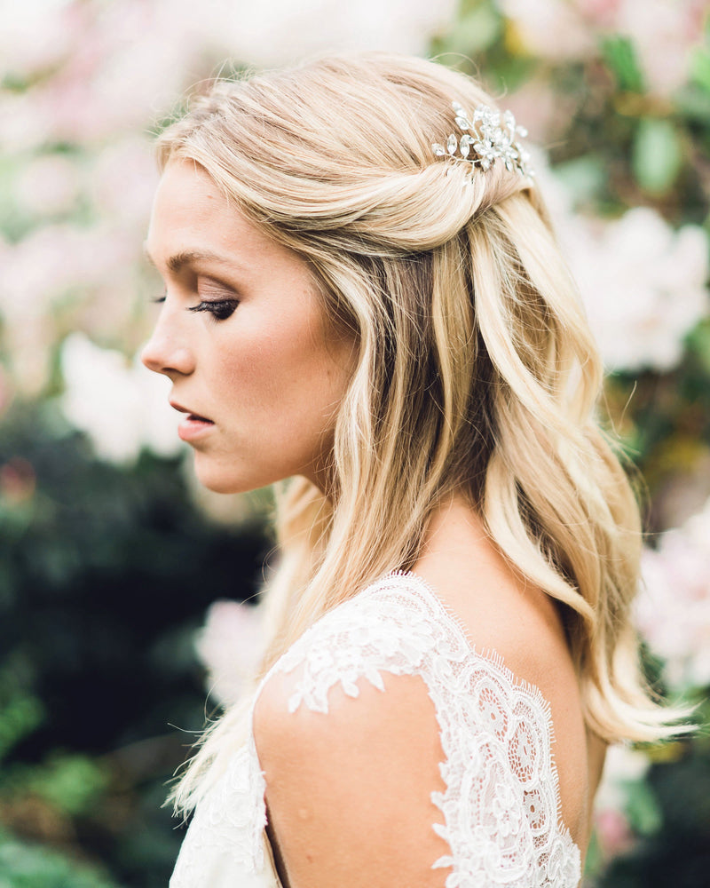 A bride wears two crystal hair pins; her hair is styled into a bridal updo of soft waves, with the sides pinned back.