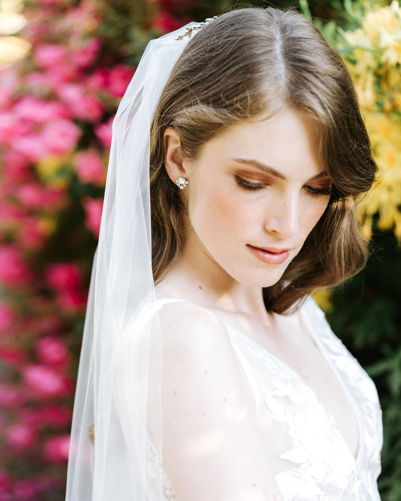 A bride stands in a flower garden. She wears a classic long veil with no trim.