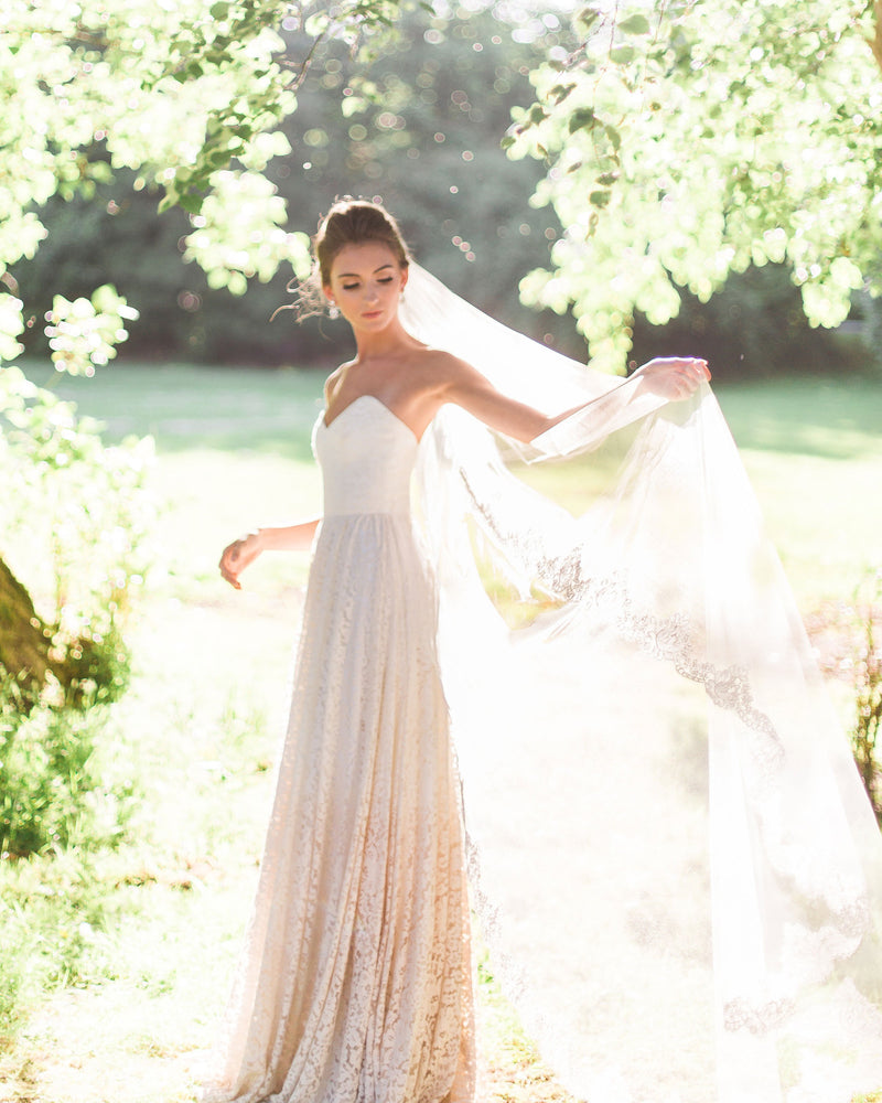 A bride stands with sunlight streaming down. She is wearing the Magnolia Lace Veil in chapel length.