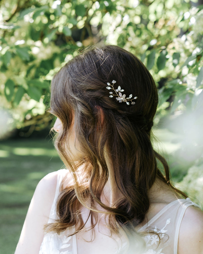 A bride with hair down and braids wears the Moonflower Comb in gold, with rose quartz gemstones, pearls, and crystals.