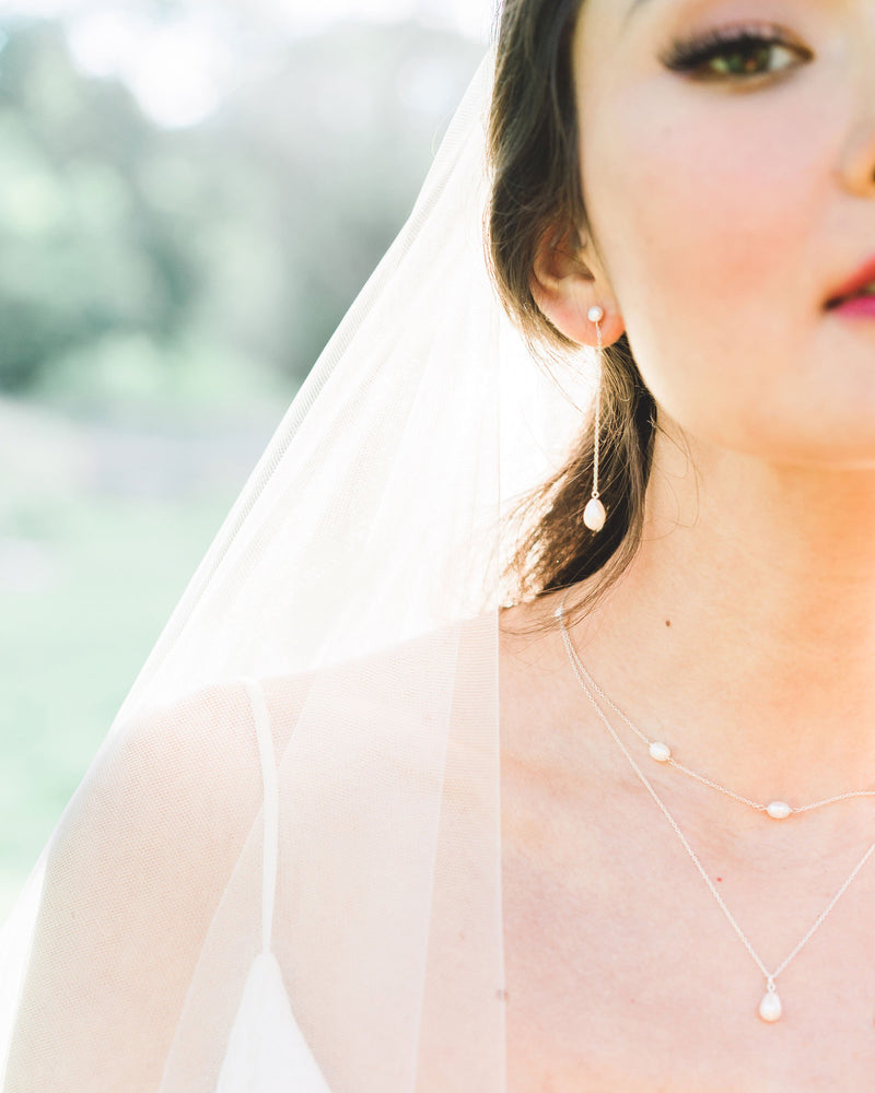 A bride wears the Teardrop Pearl Long Earrings, paired with a Layered Pearl Necklace and veil.