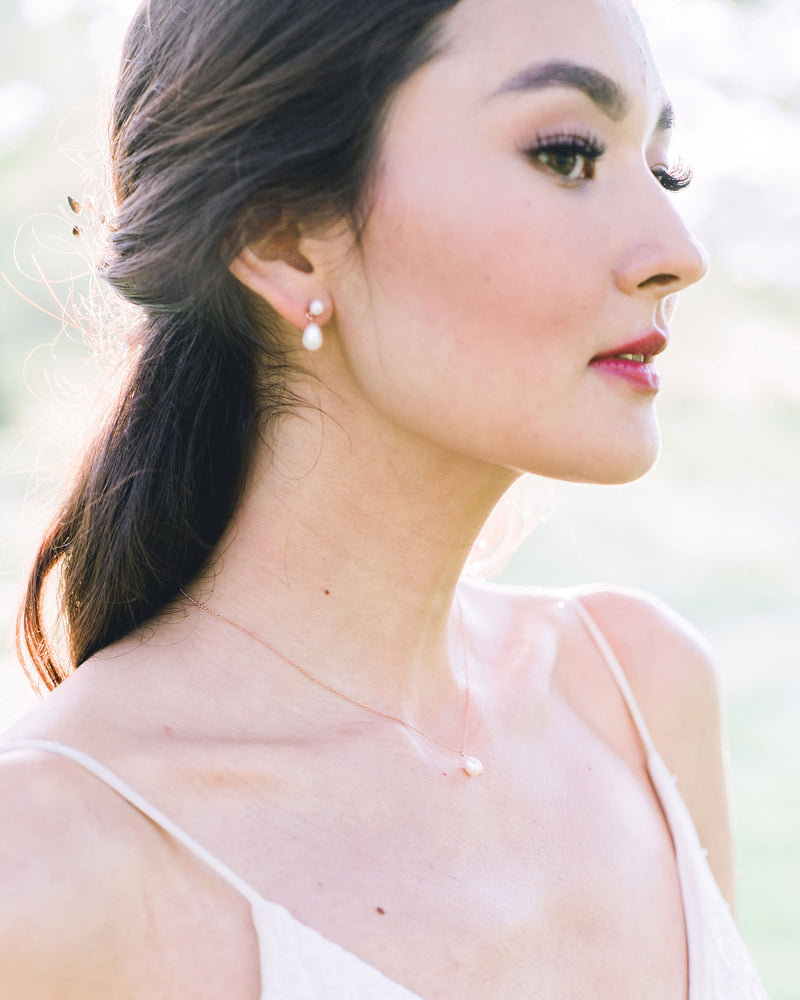 A bride wearing a classic bridal jewellery set, with petite drop earrings and matching pearl drop necklace.