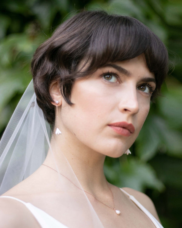 A bride with a pixie cut wears dainty flower drop earrings on a pearl stud with a matching teardrop pearl necklace..