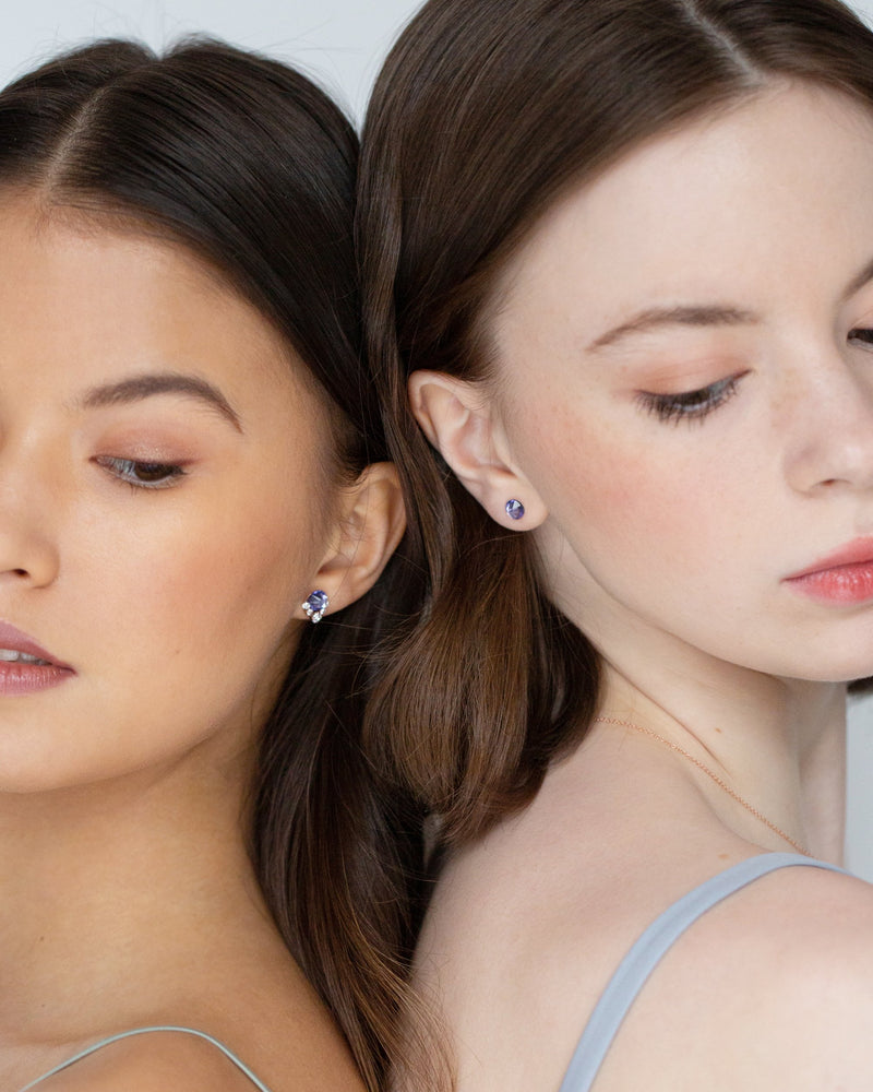 Two models wear bridesmaid jewellery. On left, she wears the Celestial Crystal Stud Earring in rose gold/tanzanite. On the right, she wears the Starry Eyed Stud Earrings in tanzanite
