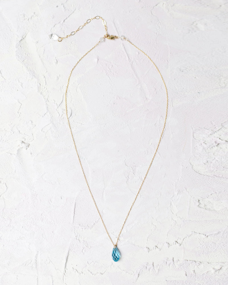 Flatlay of the Dewdrop Necklace with aquamarine crystal drop in gold.