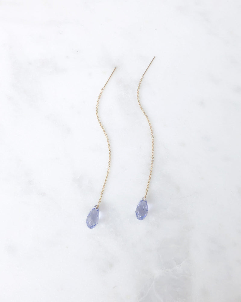 Flatlay of the Dewdrop Threader Earrings in gold with lavender crystal drops.