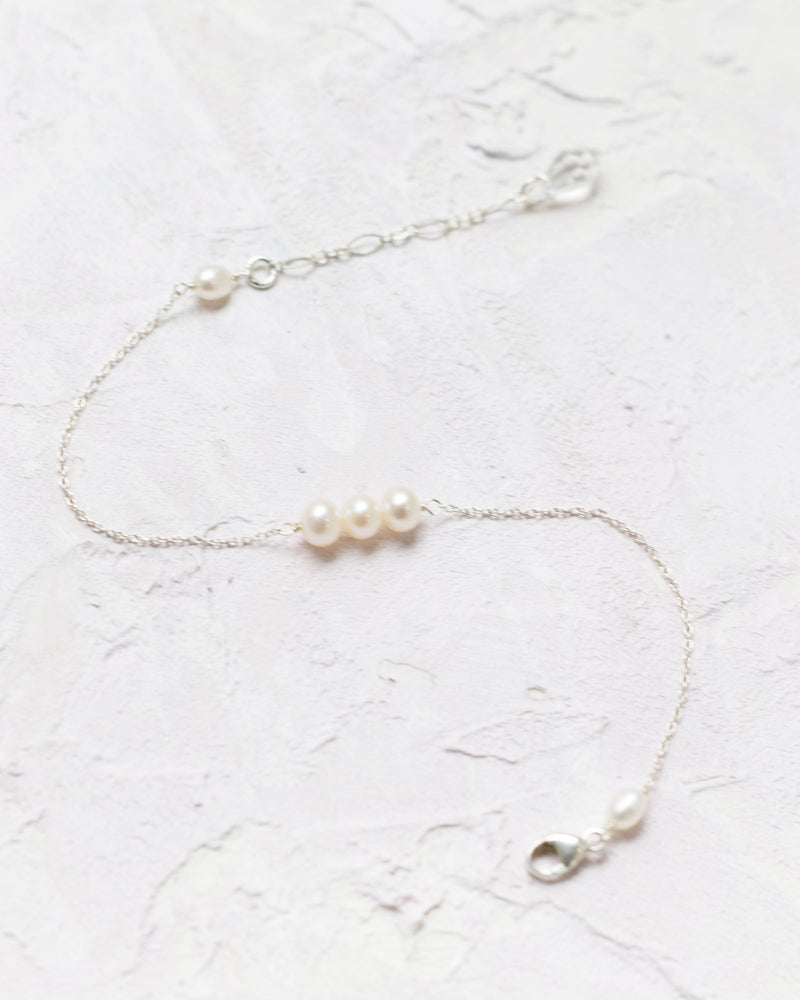 Flatlay of the Pearl Trio Bridesmaid Bracelet in silver; three freshwater pearls on a delicate chain.