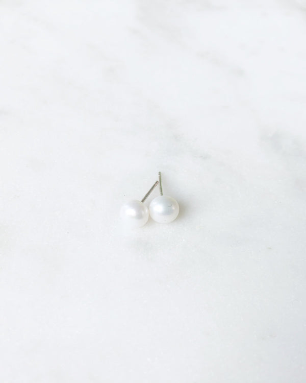 Flatlay of the Pearl Stud Earrings in petite size, shown in silver.