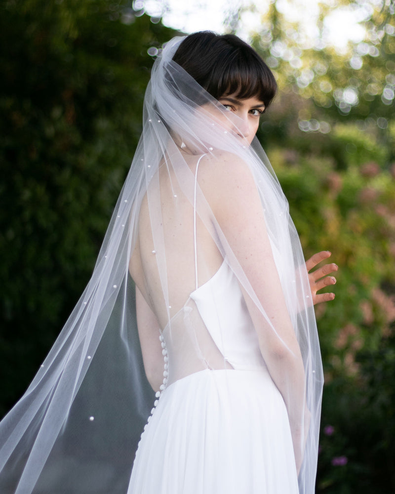 A bride wears a long veil scattered with pearls throughout the top half of the veil.