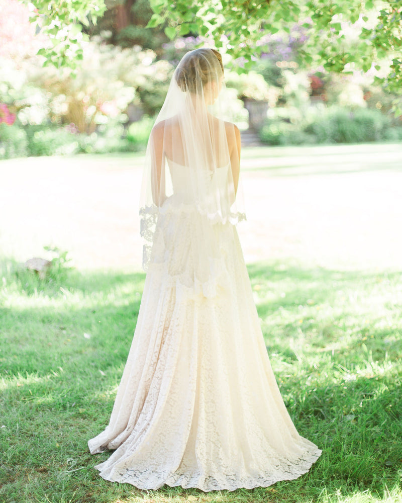 Back view of a bride wearing the Amara two-layer lace fingertip bridal veil with the blusher to the back.