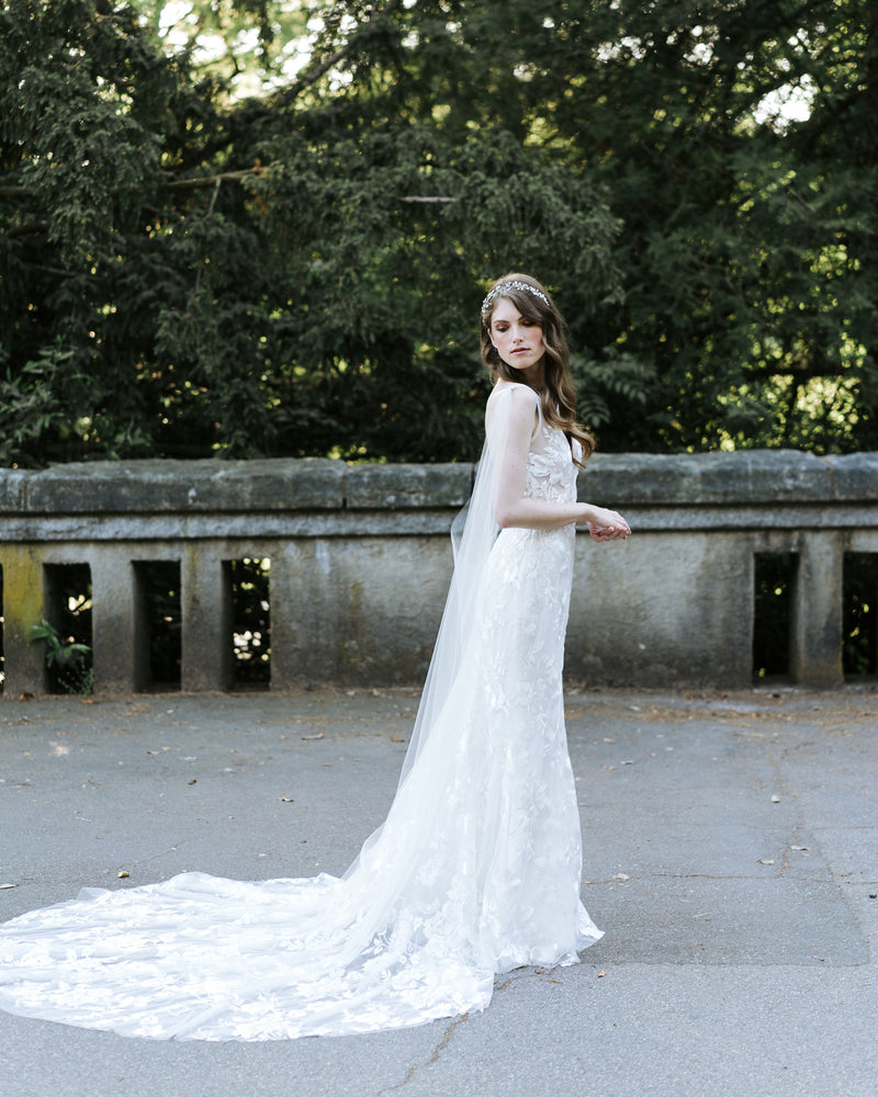 A model wearing the Aster Cape Veil, paired with a Made with Love wedding dress with a long train.