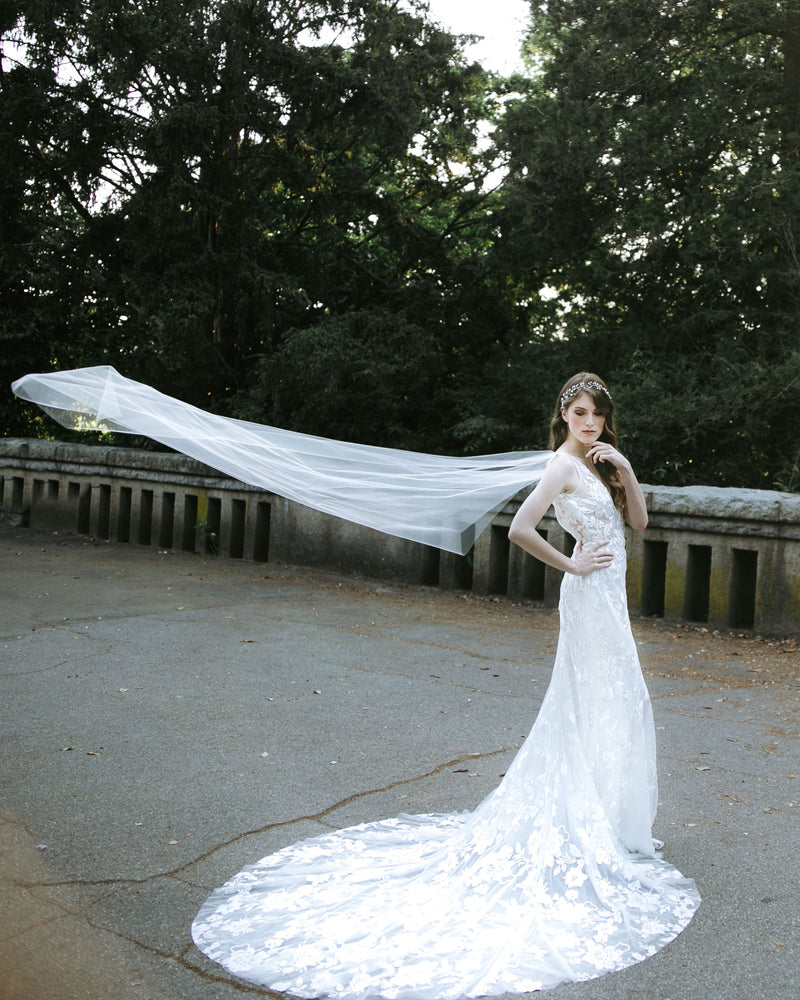 A bride poses while the Aster Cape Veil floats in the air behind her.