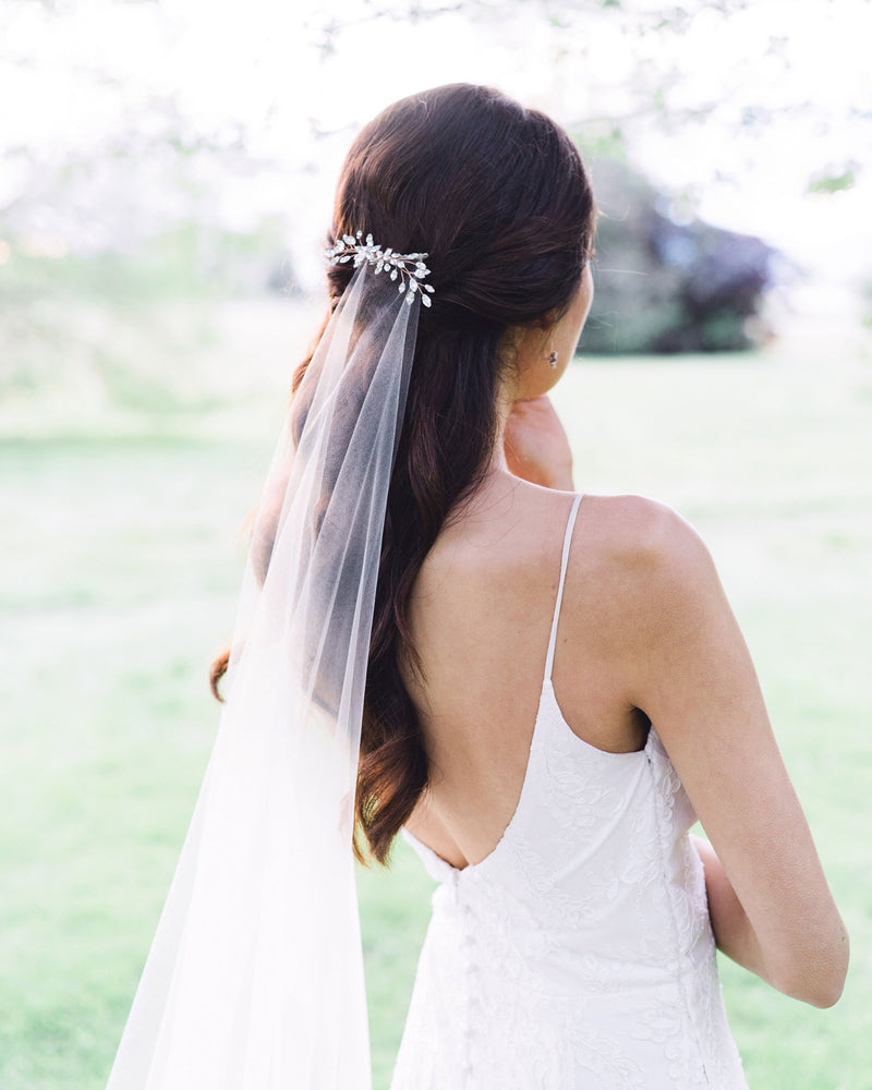 Bride with a half-up hairstyle wearing a crystal bridal hair comb over a veil.
