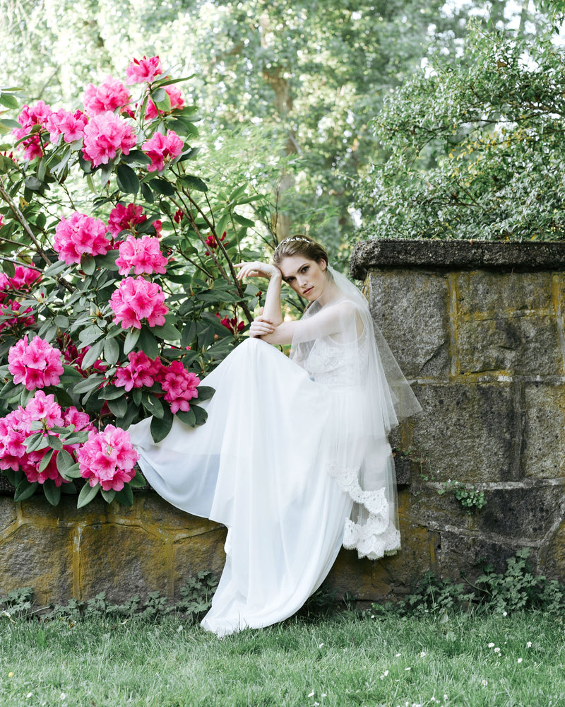 Model sitting amongst wildflowers and wearing the Azalea Alencon Lace two-layer veil.