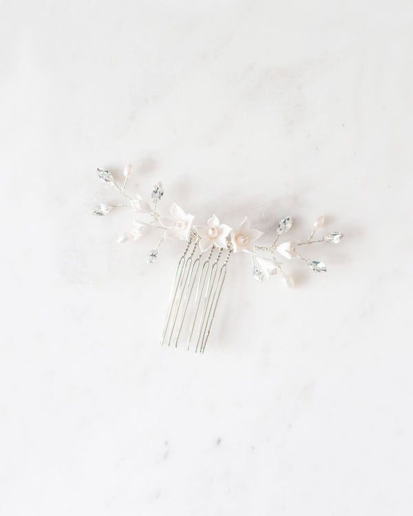Flatlay of silver bridal hair comb with crystals, white flowers, and pearls.