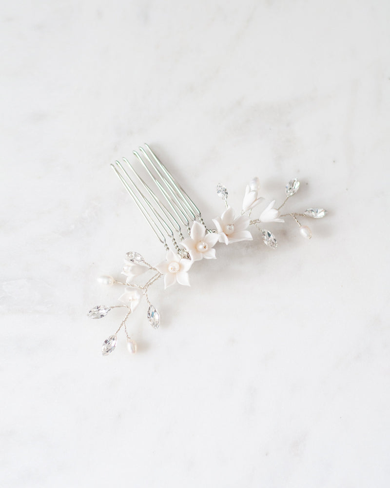 Flatlay photo of silver bridal hair comb with crystals, white flowers, and pearls.