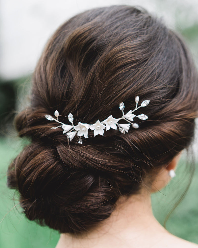 Close-up of a bride with dark hair and low updo wearing a bridal hair comb with crystals, flowers, and pearls.