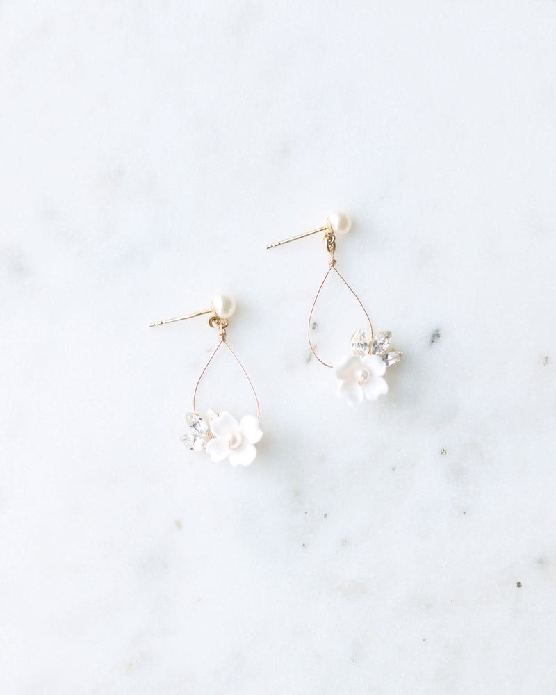 Flatlay of hand-crafted statement earrings with delicate wire teardrop. small white flower and crystals hanging from a pearl stud.