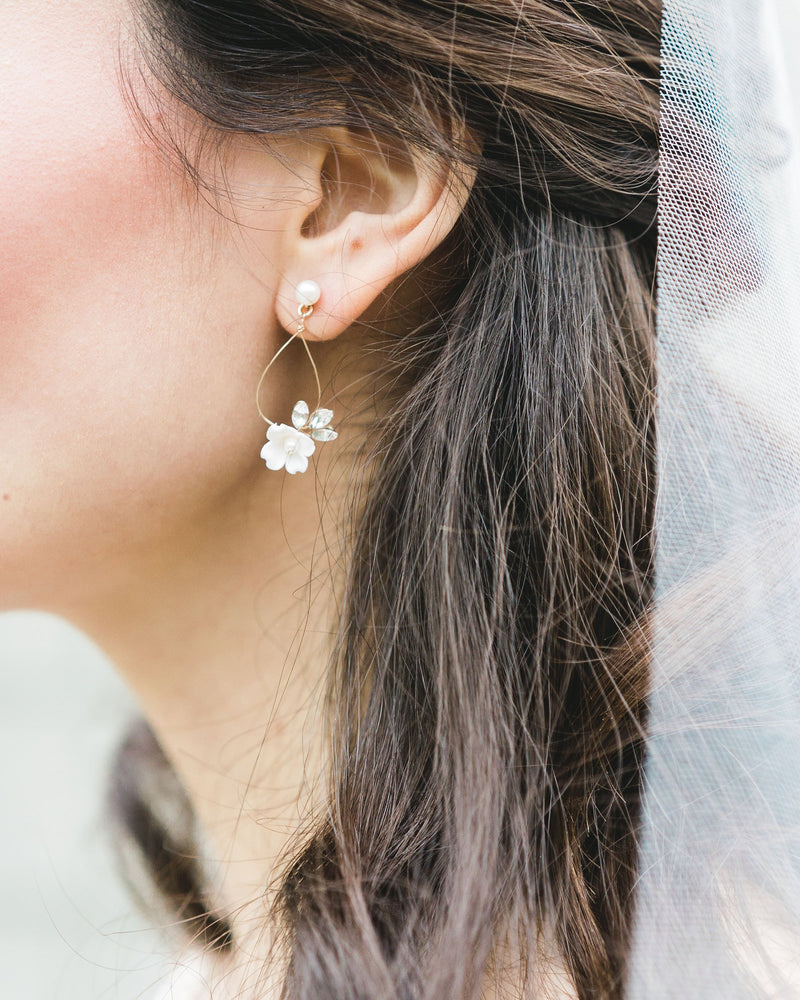 Close-up of model wearing delicate statement earring with white flower, crystals, on a wire teardrop hanging from a pearl stud.