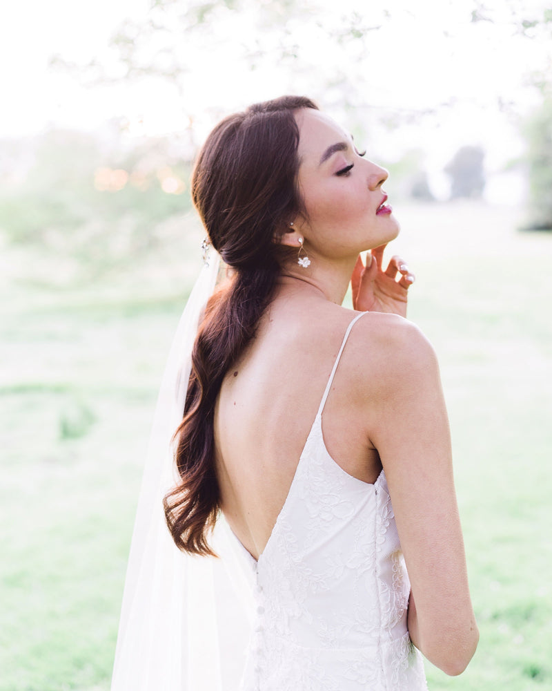 Bride posing during golden hour. She has dark hair and a dark red lip and is wearing the Belle Fleur Earrings with rose gold wire, blush flowers, and crystal accents.