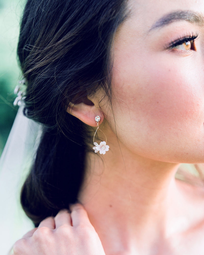 Close-up of a bride with dark hair wearing the Belle Fleur delicate statement earrings in rose gold, with blush flowers and all crystal.