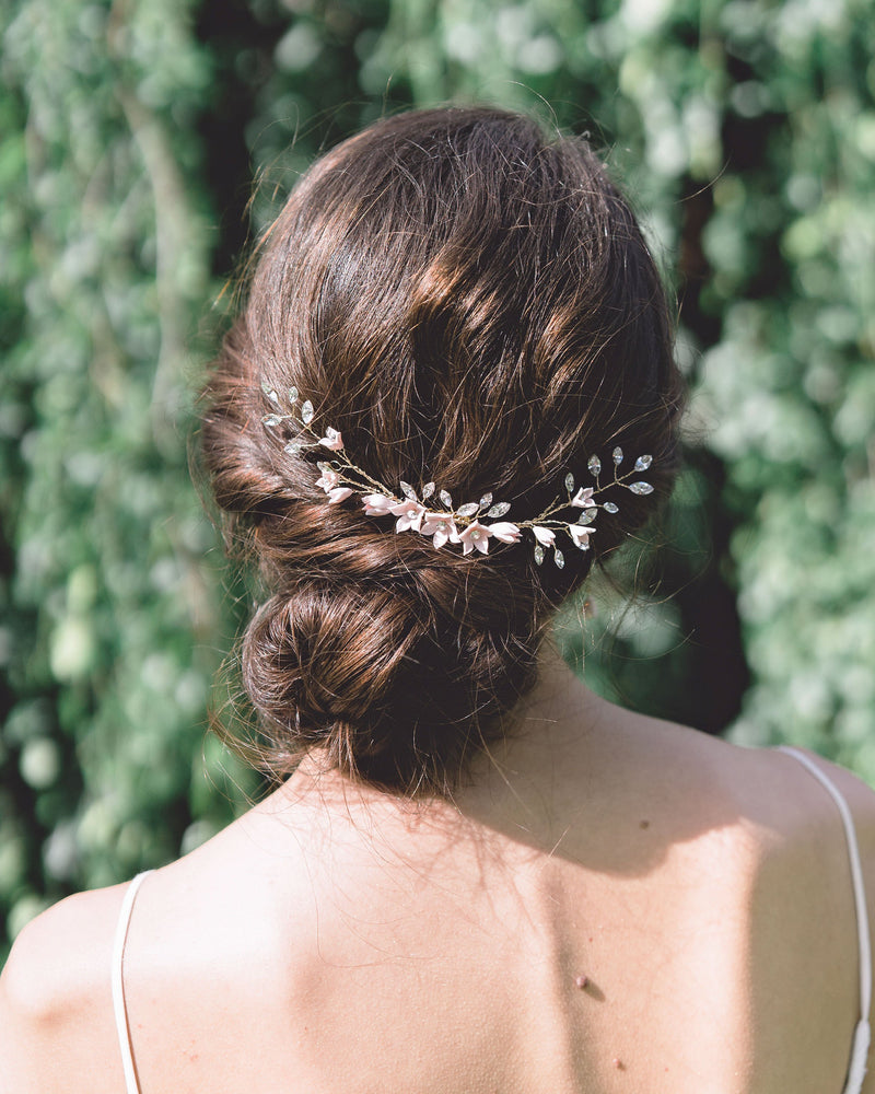 A dark-haired bride wears the Belle Fleur Grand Comb above a low bridal updo. The comb is gold with blush flowers and lots of crystals.