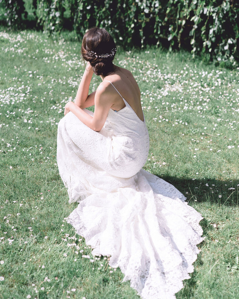 A bride poses in a grassy field. She is wearing a low bridal updo with a dramatic comb in the back.