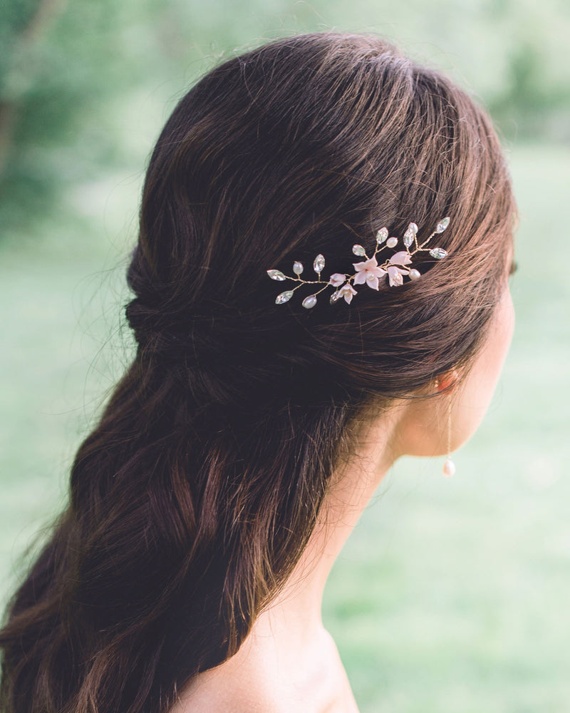 Back view of a dark-haired bride with a half-up hairstyle. She is wearing a hair pin in the side that is gold with blush flowers, pearls, and crystals.