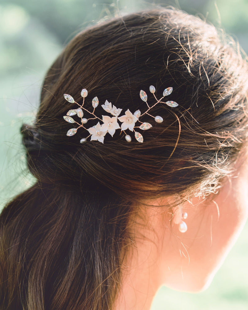 A close-up of a dark-haired bride wearing a trio of hair pins styled into her hair. The Belle Fleur Hair Pins are rose gold with blush flowers, pearls, and crystals.