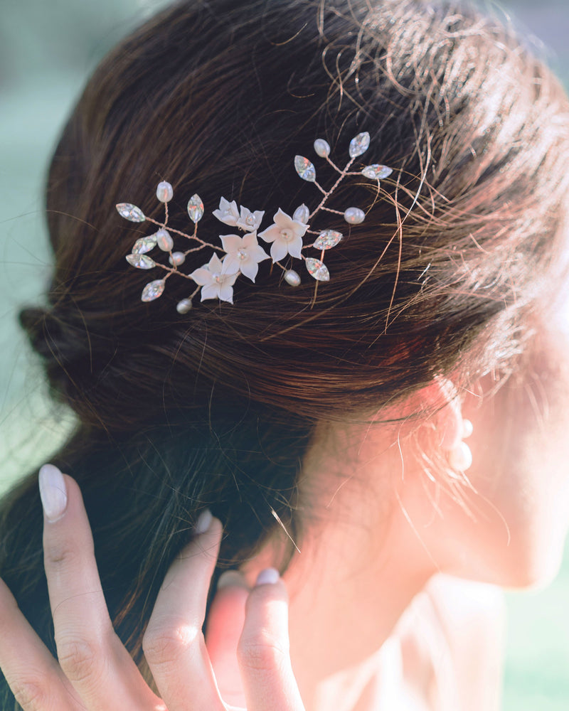 A close-up of a dark-haired bride wearing a trio of hair pins styled into her hair. The Belle Fleur Hair Pins are rose gold with blush flowers, pearls, and crystals.