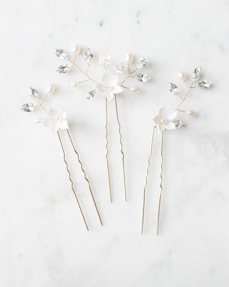 Flatlay of the trio of Belle Fleur Hair Pins. The pins are gold, with white flowers, pearls, and crystals.