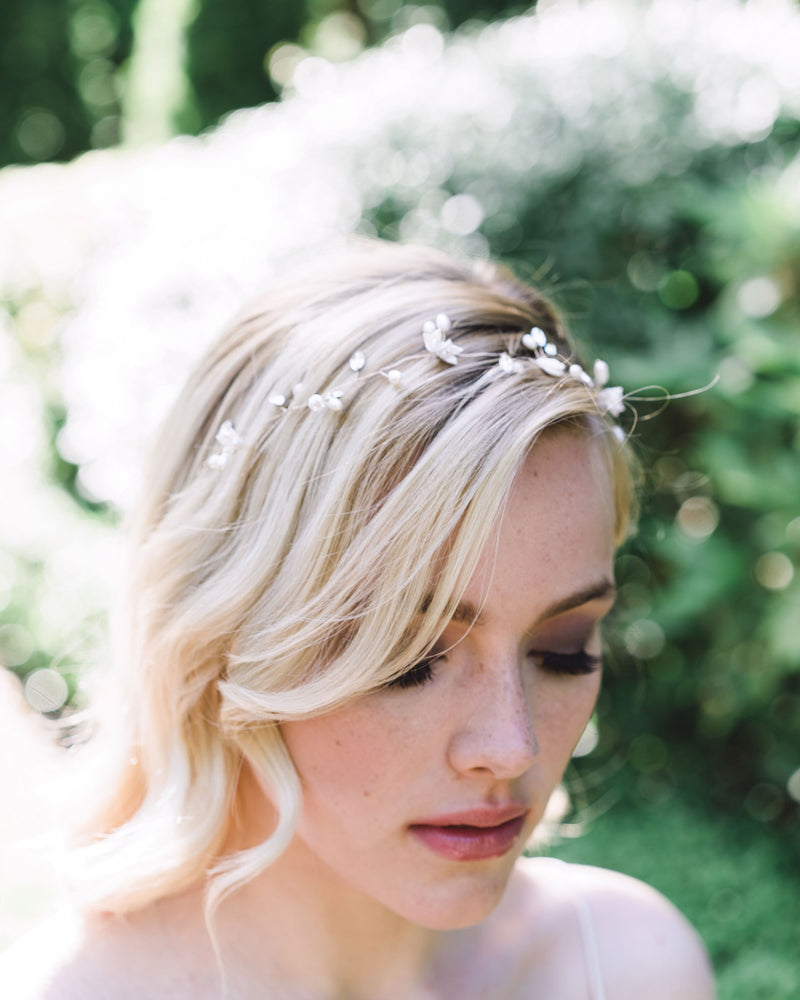 A slight top view of a model wearing the Belle Fleur Hair Vine. She is gazing downwards, and hints of dainty pearls, flowers, and crystals can be seen.
