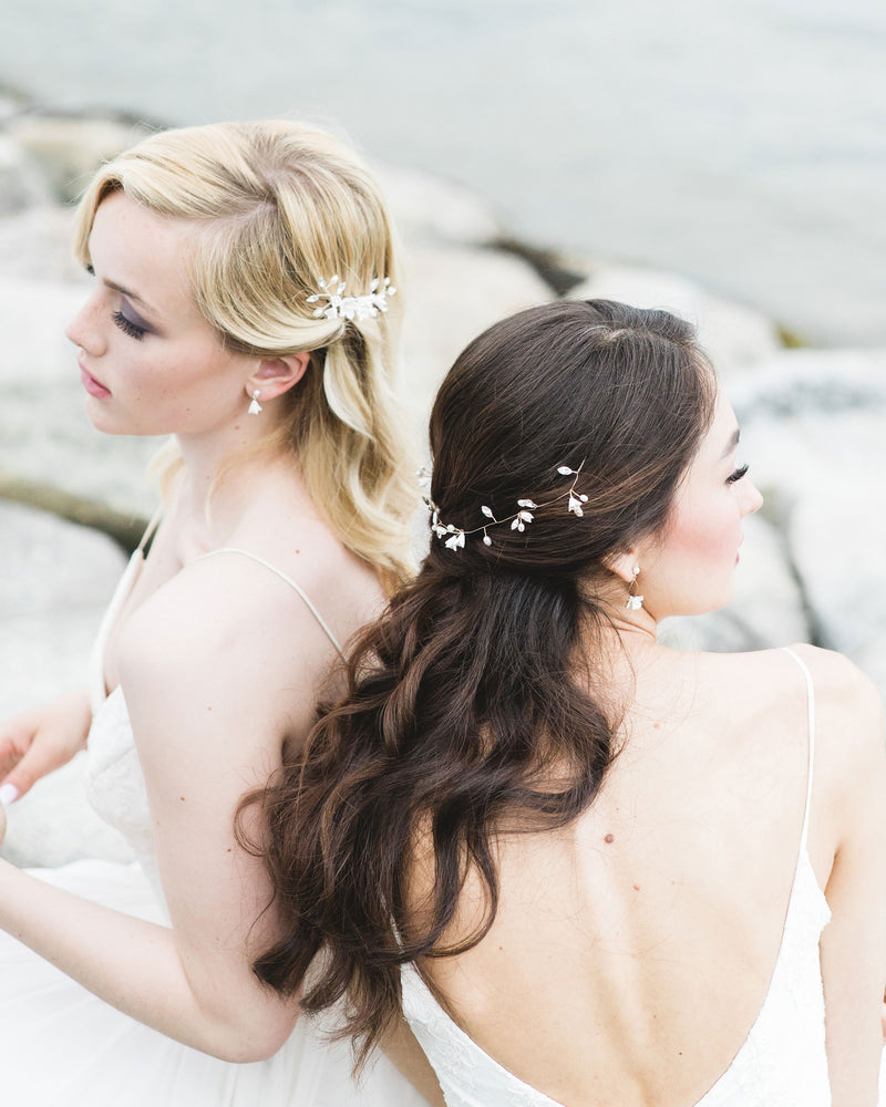 Two models pose on the rocky shore. They are wearing bridal accessories; the blonde model on the left wears small flower drop earrings and the dark-haired model on the right wears the Belle Fleur Hair Vine styled across the back of her half-up hairdo.