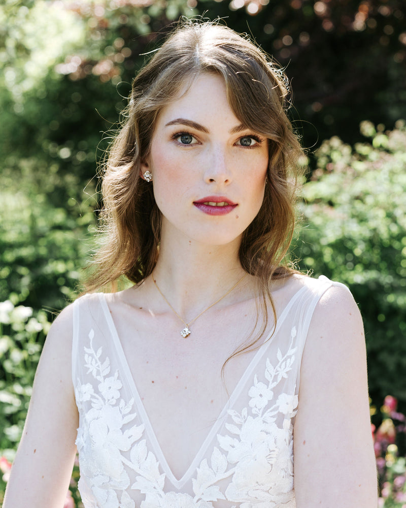 An auburn-haired bride is wearing a delicate crystal jewellery set. She wears crystal stud earrings and a delicate gold necklace with a crystal drop