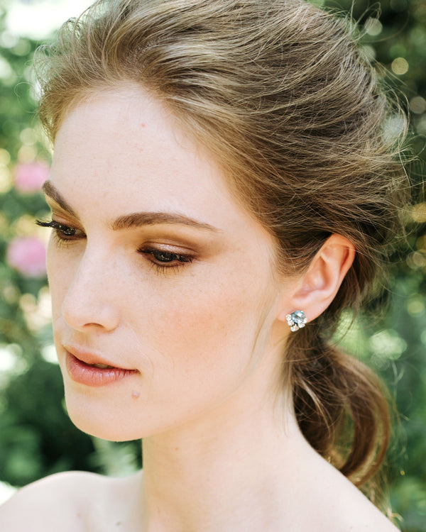 A model with a bridal updo wears silver crystal stud earrings with aquamarine crystals above a cluster of smaller crystals.