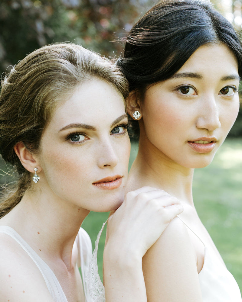 Two brides are wearing wedding jewellery. On left, she wears the Celestial Crystal Drop Earrings in silver; on right, the model wears the stud version in silver/crystal.