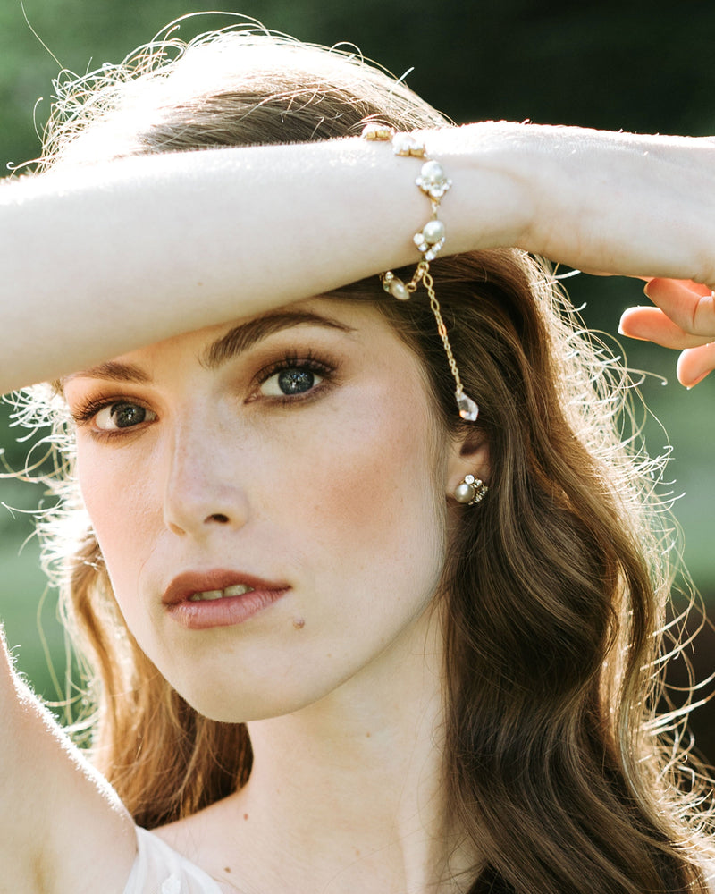 A bride wears the Celestial Pearl Cluster Bracelet in gold and matching pearl stud earrings.