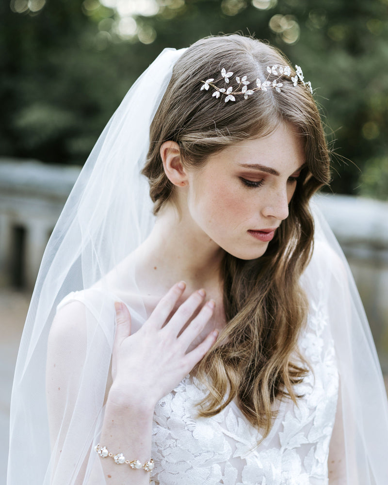 A bride with auburn hair wears a floral bridal headpiece with crystal leaves, a pearl and crystal bridal bracelet and a soft tulle veil.
